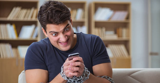 A man with hands chained together holds a phone. He has a crazed look in his eye as he stares at the screen. This is exactly how we looked like when we wrote this blog post.